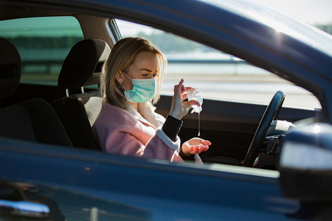 vrouw in auto met mondkapje en ontsmettingsmiddel